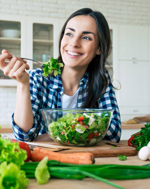 young woman sitting at table with large bowl salad for detoxification health